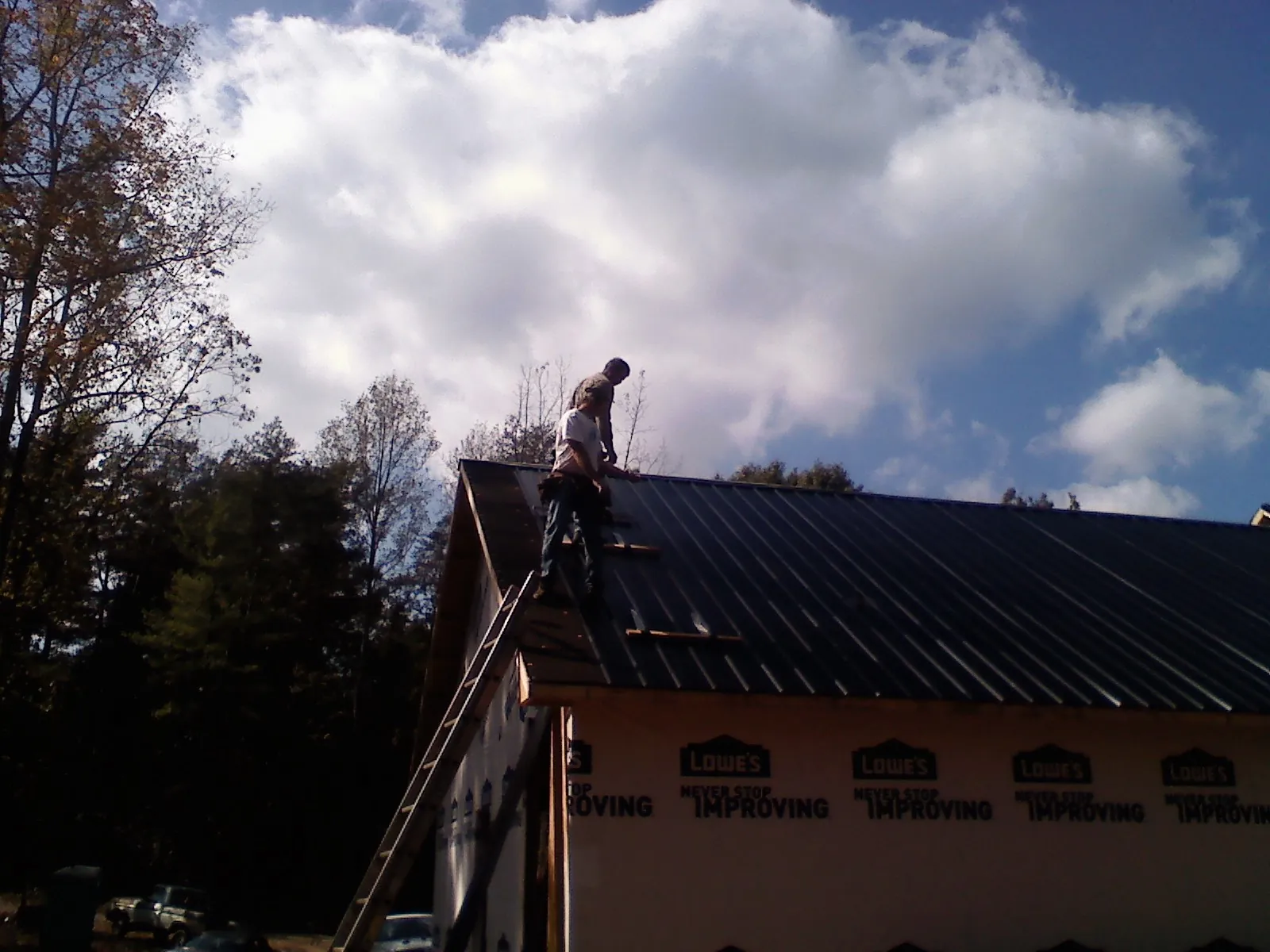 Roofer fastening dark metal panels high against a cloudy sky, from a Roof Inspection job in Seal Rock