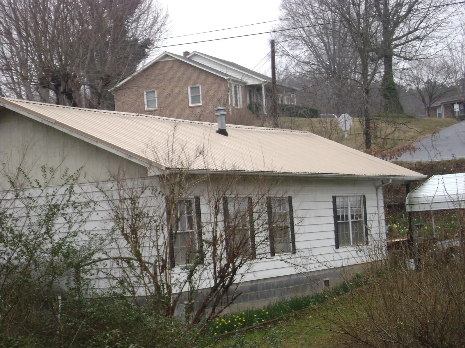 Tan metal roof on a white sided house set into a hillside — Commercial Roofing by Roofing Brothers in Seal Rock